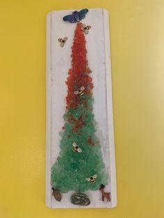 a small christmas tree made out of gummy bears and other items on a yellow background