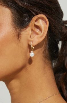 a woman wearing a pair of earrings with pearls on the end of her ear, looking off to the side