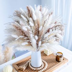 a white vase filled with feathers sitting on top of a wooden tray