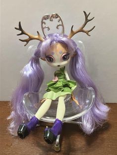 a doll sitting on top of a glass plate with deer antlers around her head