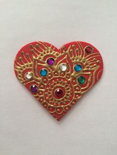 a red and gold heart shaped brooch with jewels