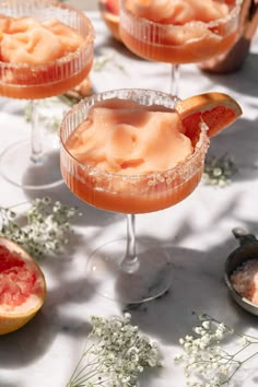 three glasses filled with drinks and garnished with grapefruit on a table