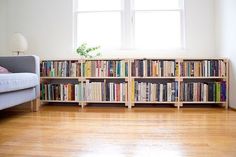 a living room with a couch, book shelf and window in the corner that has books on it