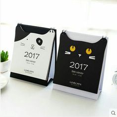 two black and white cat calendars sitting on top of a table next to a cup