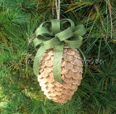 a pine cone ornament hanging from a tree with a green bow on it