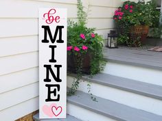 a wooden sign that says be mine on the side of a house next to some flowers