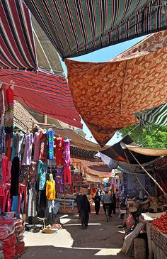 an outdoor market with lots of umbrellas and people walking around it on a sunny day