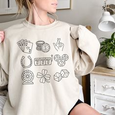 I'd Rather be at the Casino! This gambling shirt featuring a lucky 7 ball, shamrock, horseshoe and other lucky charms would be perfect for a casino theme party, casino retirement, or gambling gift. If you or your loved one is probably at the casino, then this is the cozy, comfy sweatshirt for you!  -Unisex, heavy blend crewneck sweatshirt -Made from 50% polyester and 50% cotton -Ribbed knit collar retains shape -No itchy side seams or tags (label is sewn-in) -Loose fit is true to size  FREE SHIPPING! Printed in the USA -------SIZING------- Please consult the size chart in the listing images carefully for fit. If you want an oversized look, consider sizing 1-2 sizes up. -------SHIRT COLORS------- Please see images for different colors offered. Note: white can appear grey or faded on darker Casino Theme Party Outfit Women, Casino Theme Party, Gambling Gift, Party Outfits For Women, Lucky 7, Balls Shirt, Merch Ideas, Casino Outfit, Casino Theme