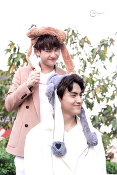 two people standing next to each other with stuffed animals on their heads and one person holding an umbrella over his head