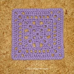 a purple crocheted square with hearts on it sitting on the floor in front of a carpet