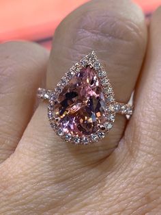 a woman's hand holding an engagement ring with a pink diamond in the center