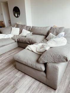 a large gray couch sitting in a living room next to a wooden floor and white walls