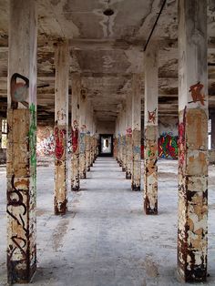 an abandoned building with graffiti all over the walls and floor, along with pillars in between