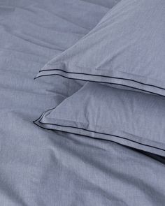 two pillows sitting next to each other on top of a blue bed sheet with black piping