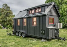 a tiny house is parked in the middle of a grassy field with trees around it