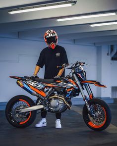 a man standing next to a dirt bike in a parking garage with his helmet on