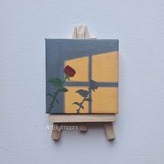 a small easel with a painting of a red rose in front of a window