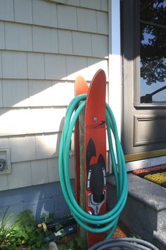 an orange surfboard and blue hose are in front of a house with a door