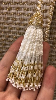 the beaded tassel is being held up by someone's hand with gold and white beads on it