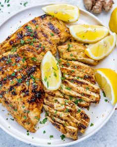 grilled chicken with lemons and parsley on a white plate next to garlic