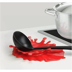 a spoon with red liquid on it sitting next to a pot and spatulas