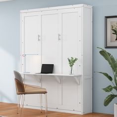 a room with a chair, desk and white cupboards on the wall next to a potted plant