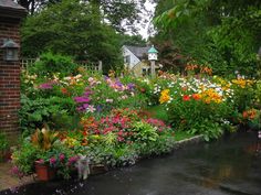 a garden filled with lots of colorful flowers next to a brick building and water feature