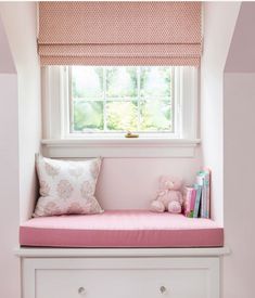 a window seat with a pink pillow and some books on the shelf next to it