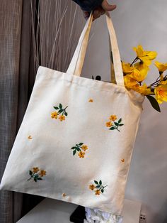 a person holding a white bag with yellow flowers on it and the bottom half of the bag