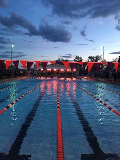 an outdoor swimming pool with red and white flags hanging from the sidelines at dusk