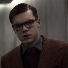 a young man wearing glasses and a suit in a dark room with light coming from the ceiling