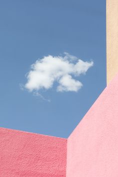 a white cloud is in the blue sky above some pink and yellow walls with two different colors