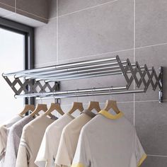 a rack with clothes hanging on it in front of a window next to a tiled wall