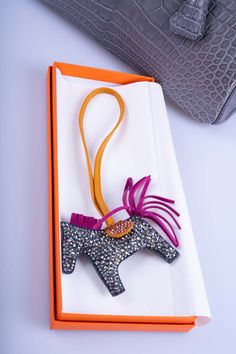 The Hermès Rodeo bag charm, already a symbol of luxury and craftsmanship, gains an additional layer of exclusivity and glamour in its customized version from the JaneFinds Custom Shop. This particular rendition is elevated with the meticulous embroidery of Swarovski crystals, enhancing its unique appeal. The sparkling crystals add a dazzling touch to the charm, making it not just an accessory but a statement piece. This customization perfectly blends the charm's whimsical design and Hermès' equestrian heritage with a modern, luxurious twist, offering an accessory that is both playful and opulent. The combination of Hermès' renowned craftsmanship in the Rodeo charm with the exquisite detailing from JaneFinds Custom Shop creates a truly bespoke piece. It's an exemplar of how traditional luxu Hermes Charm, Hermes Bag Charms, Hermes Keychain, Hermes Bag Charm, Hermes Rodeo Charm, Hermes Fine Jewelry, Hermes Dog Collar, Charmed Characters, Hermes Accessories