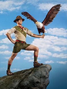 a man holding an eagle while standing on top of a rock in front of a blue sky