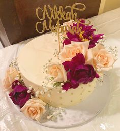 a white cake with purple flowers and a gold nameplate on top that says nikka wedding