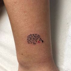 a small hedgehog tattoo on the right arm and wrist, it is black with red dots