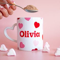 a person spooning sugar into a coffee mug with hearts and the word oliva on it