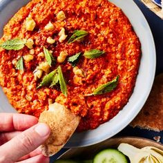 a hand dipping some bread into a bowl of hummus and other food on the side