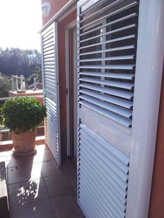 an open door on the outside of a building with shutters and potted plant