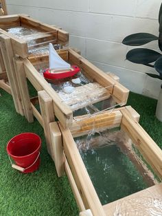 two wooden boats sitting on top of green grass next to a red bucket filled with water