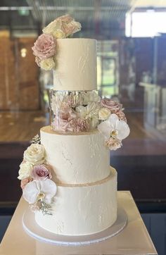 a three tiered wedding cake with flowers on it's side and frosting