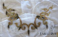 an intricately designed piece of cloth on top of a white sheet with gold thread