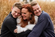 two men and a woman hugging each other in front of some tall grass with trees behind them