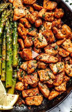 chicken and asparagus in a skillet with lemon wedges