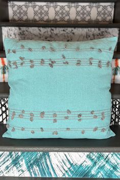 a blue pillow sitting on top of a wooden bench next to pillows and blankets in the background