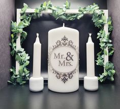 a couple of candles sitting next to each other on top of a table with greenery