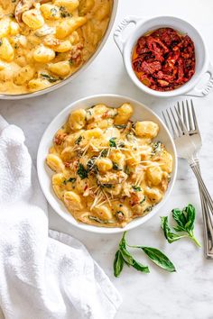 two bowls filled with pasta and sauce next to silverware on a white counter top