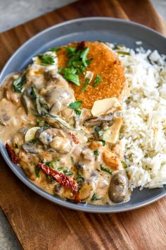 a blue plate topped with rice and meat covered in gravy on top of a wooden cutting board