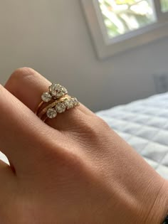 a woman's hand holding a ring with three diamonds on it, in front of a window